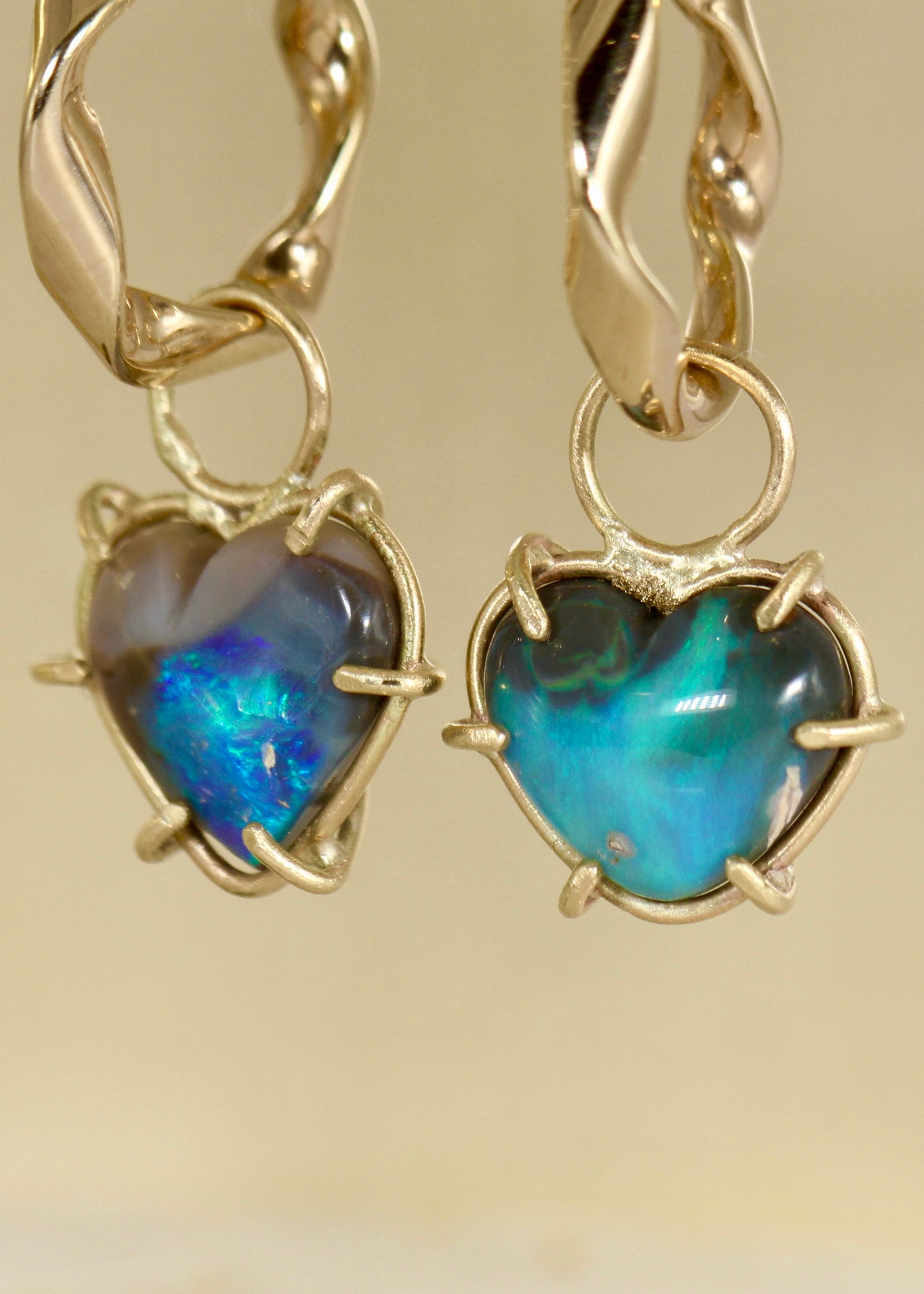 Gold heart-shaped earrings with Black and blue opal gemstones on a gold background