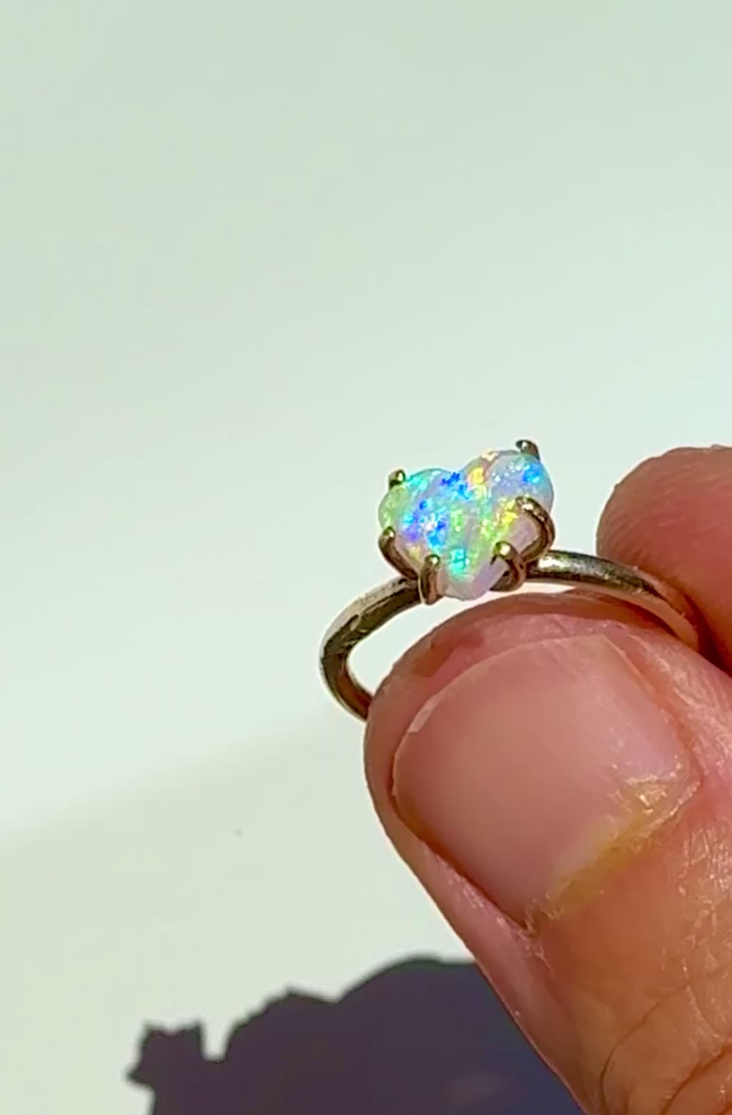 Holding the Rainbow Heart natural Australian crystal opal solid gold ring in the sunlight.