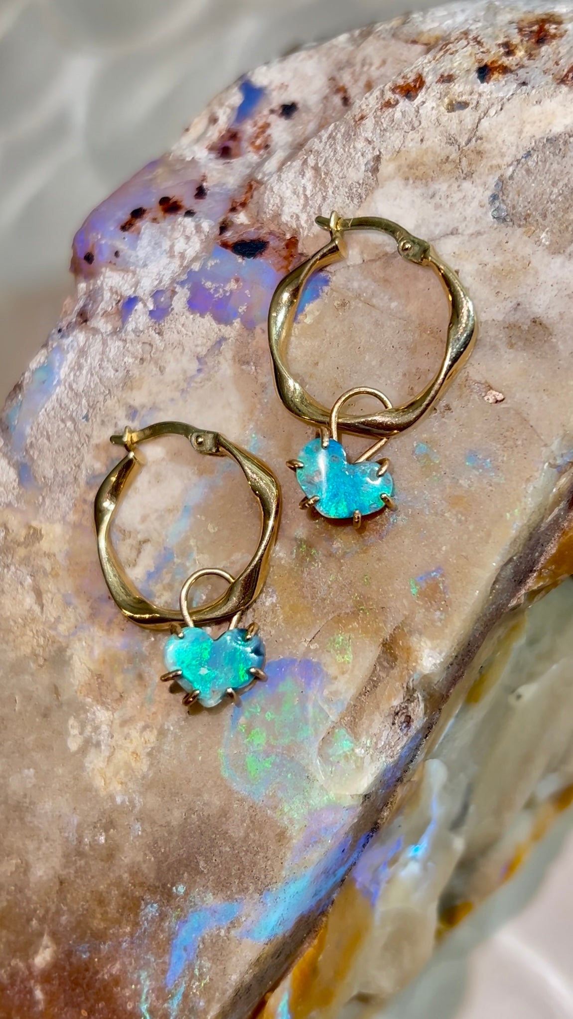 Gold hoop earrings with blue gemstones on a stone background