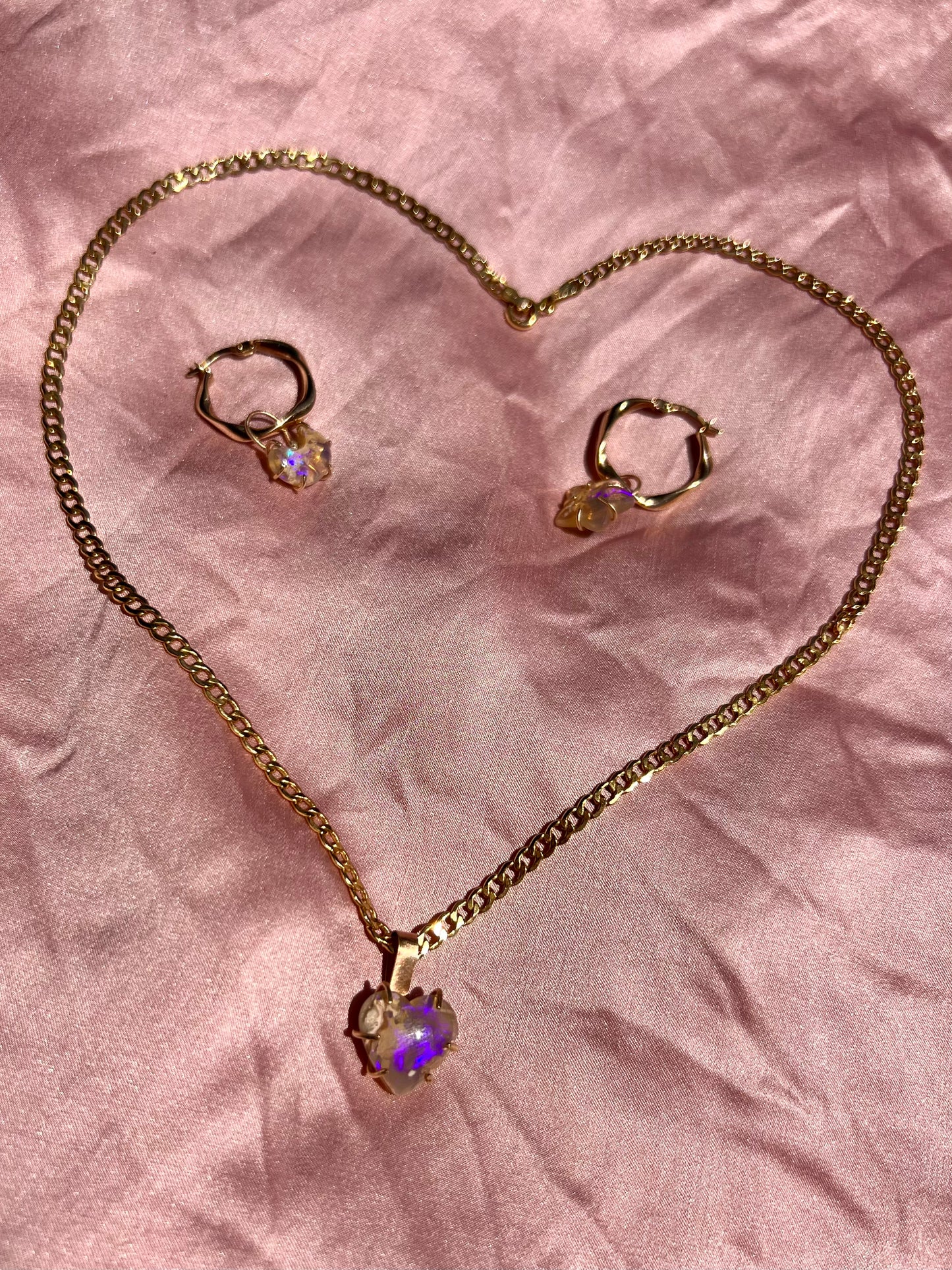 Gold necklace with pendant and two rings on a pink textured fabric background