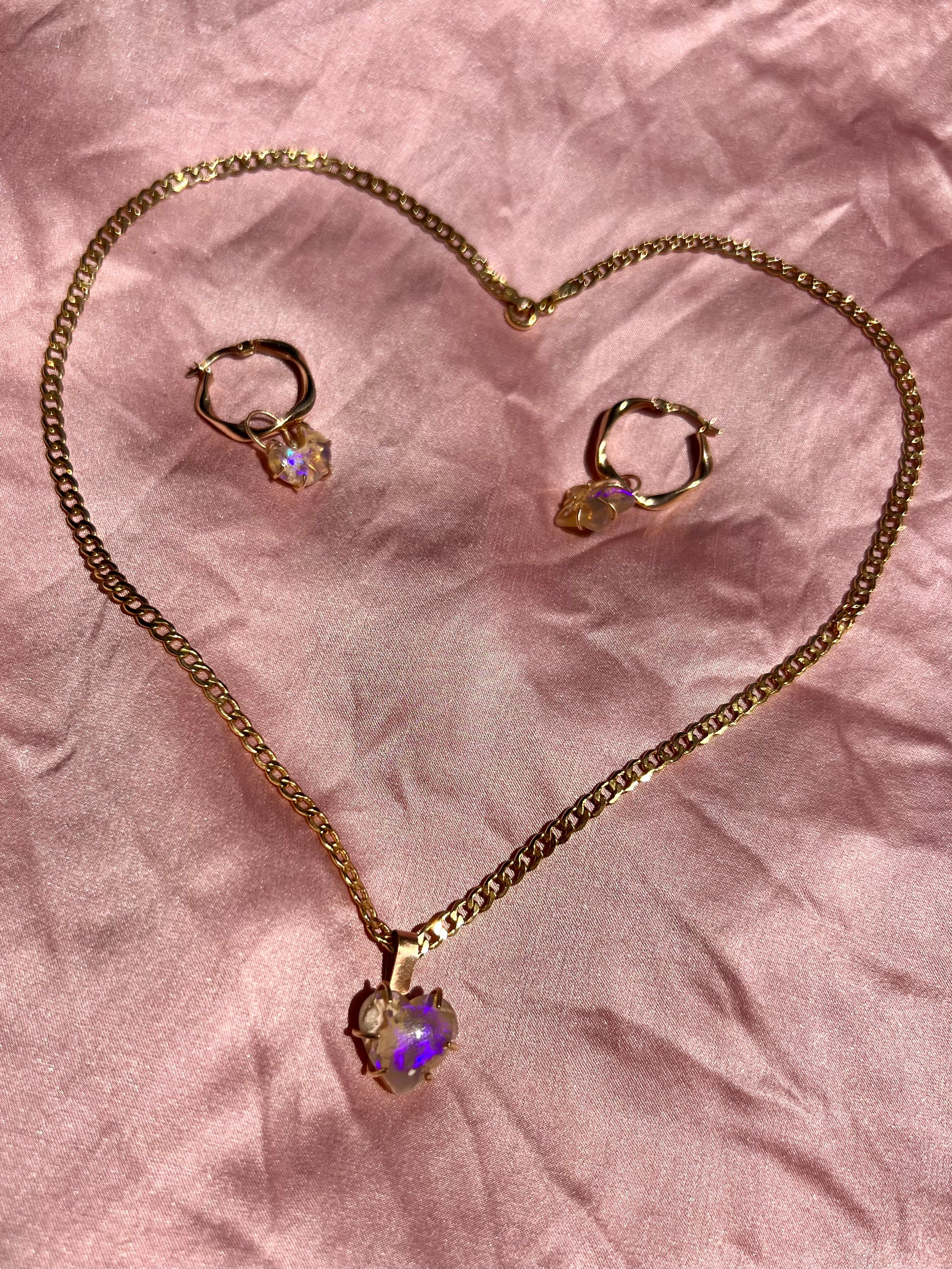 Gold necklace with pendant and two rings on a pink textured fabric background