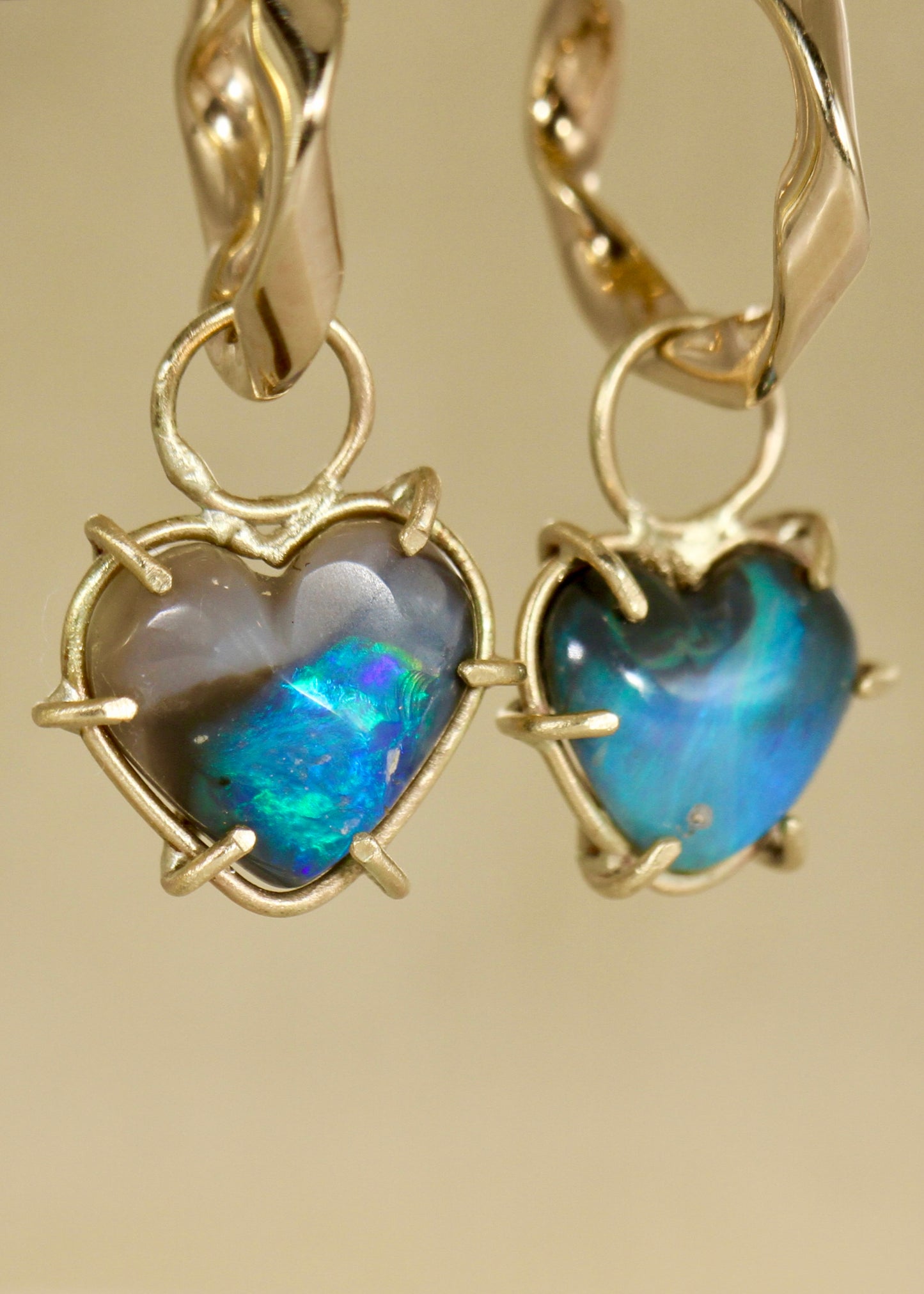 Gold heart-shaped earrings with black opal stones on a beige background