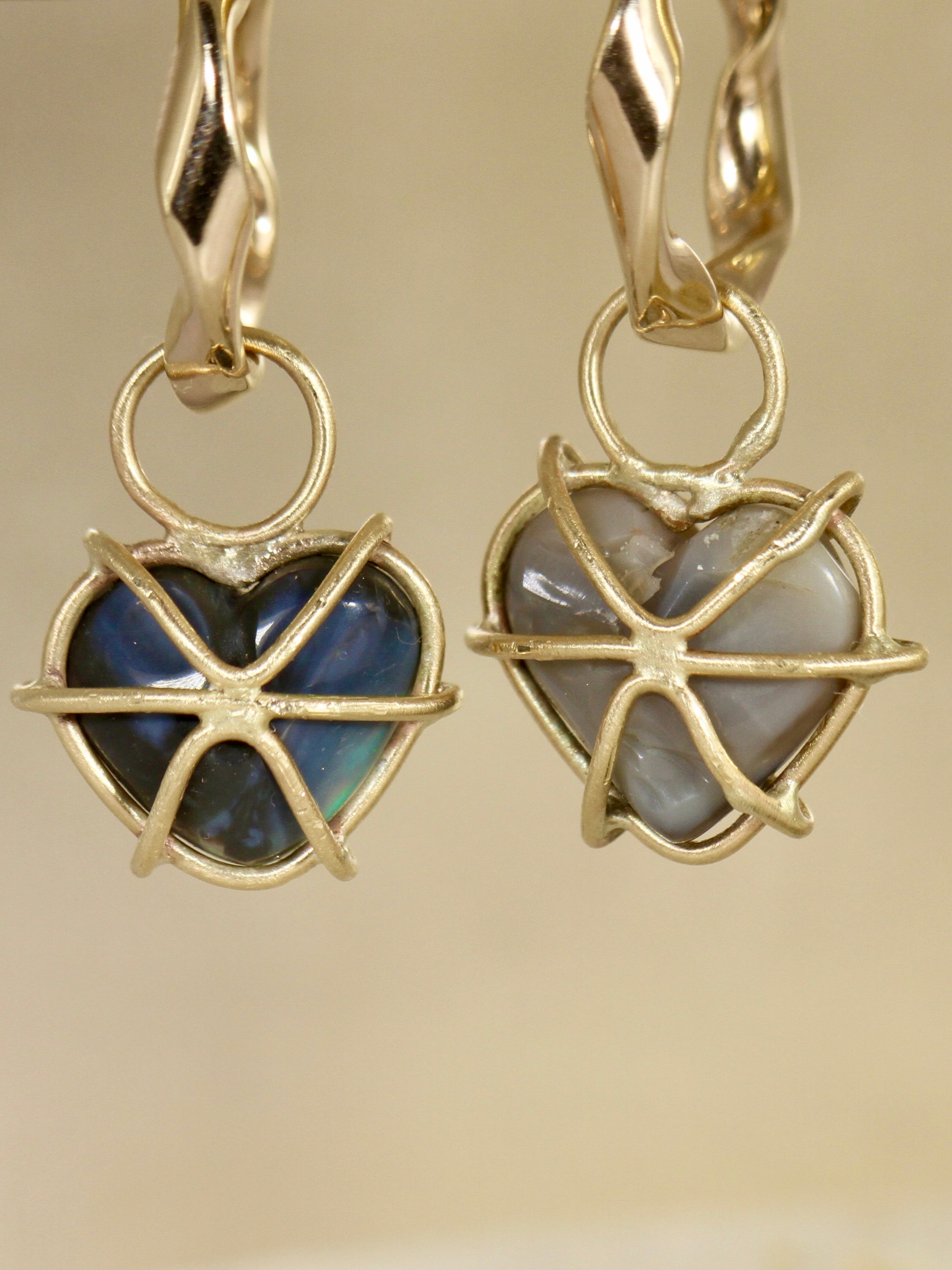 Back View of Gold heart-shaped earrings with black opal gemstones on a beige background