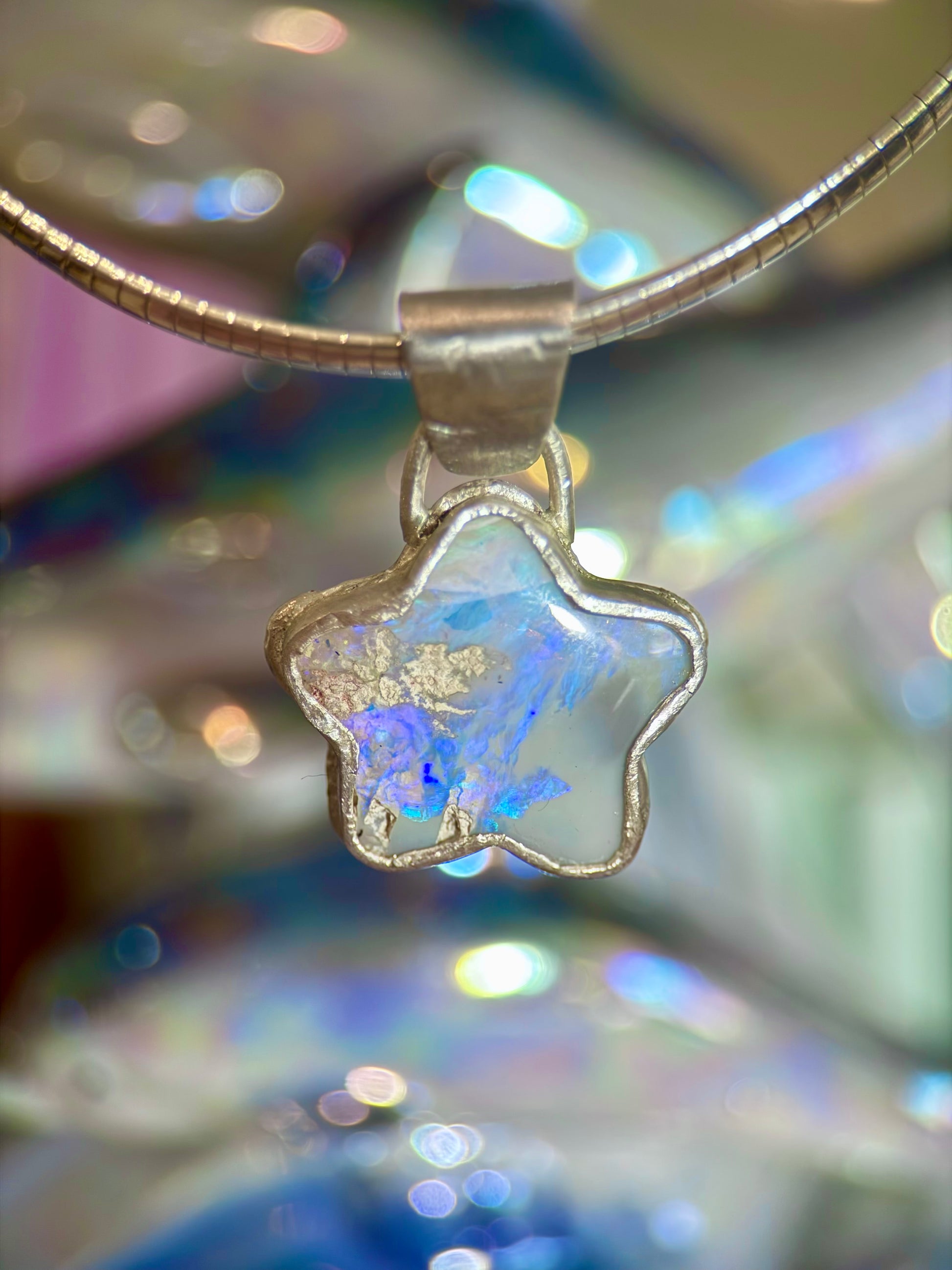 Star-shaped blue purple opal pendant on a blurred background