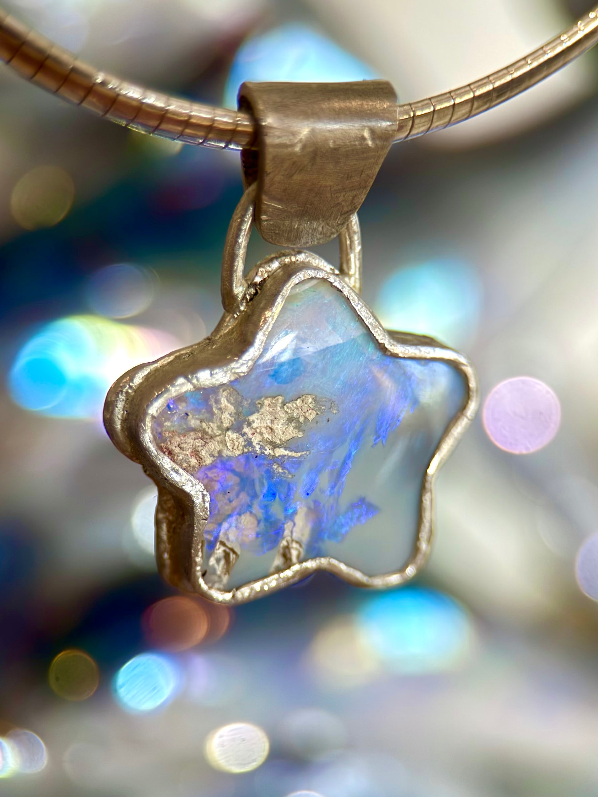 Star-shaped opal pendant with iridescent blue and purple colors on a blurred background