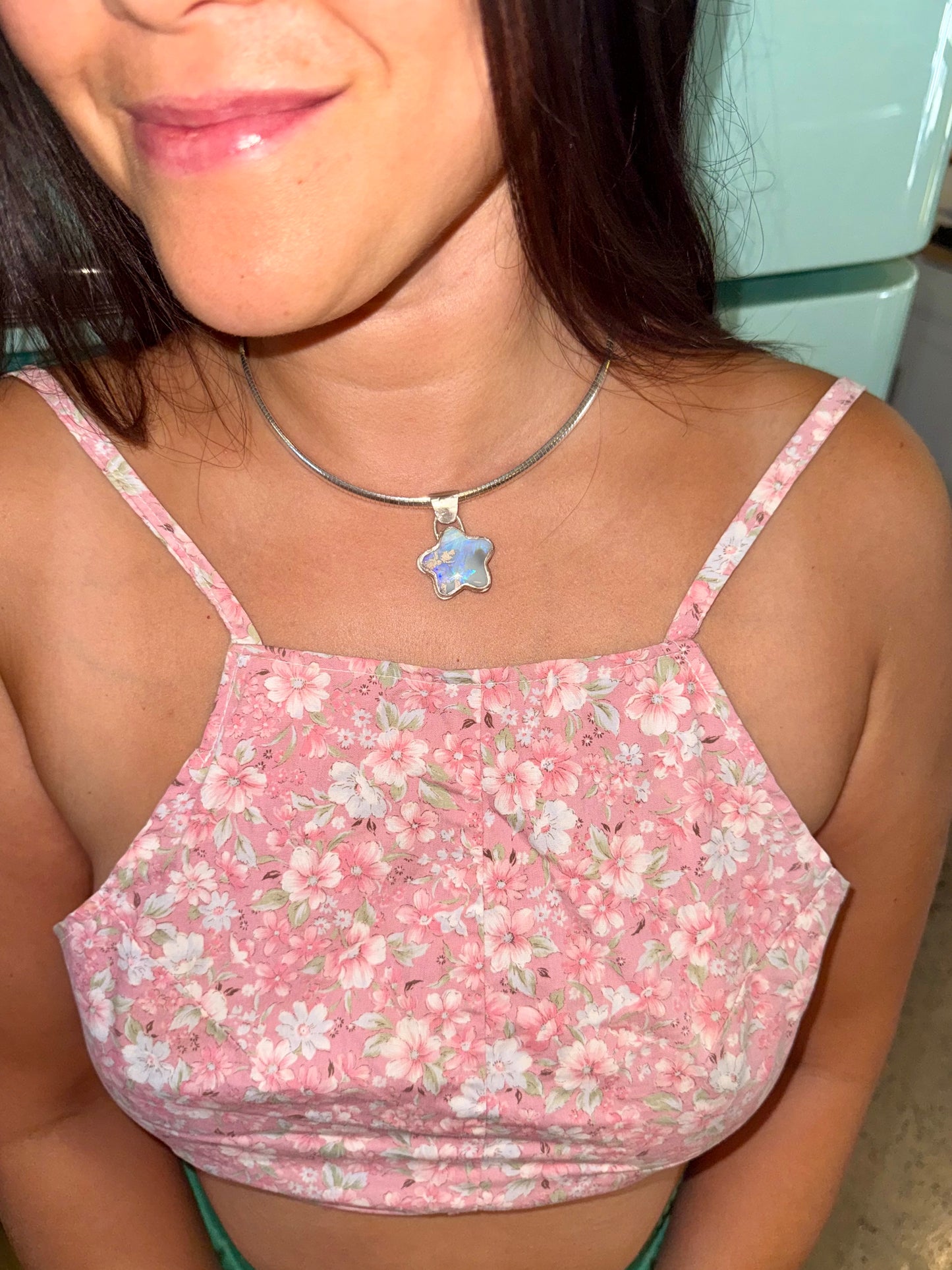 Person wearing a pink floral top with a star-shaped pendant necklace.