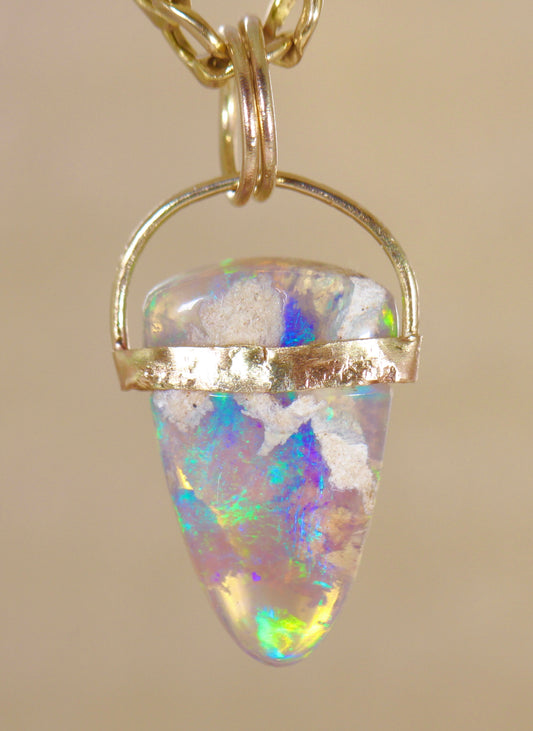 Unicorns Horn Opal pendant with gold setting on a beige background