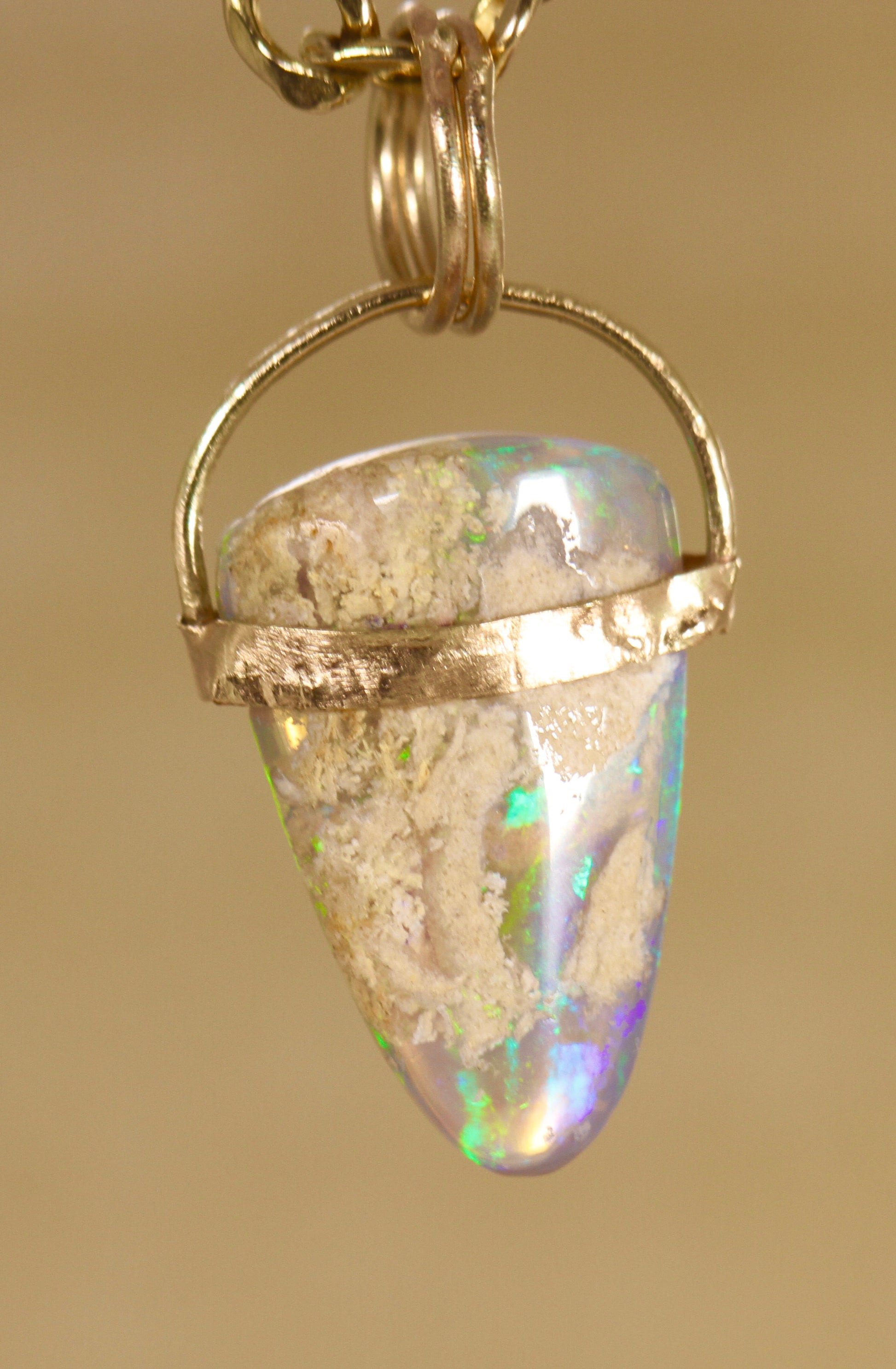 Opal pendant with gold setting on a beige background