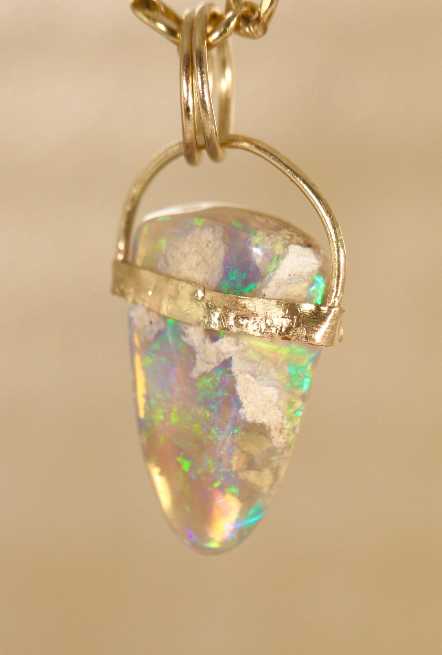 Opal pendant with gold setting on a beige background
