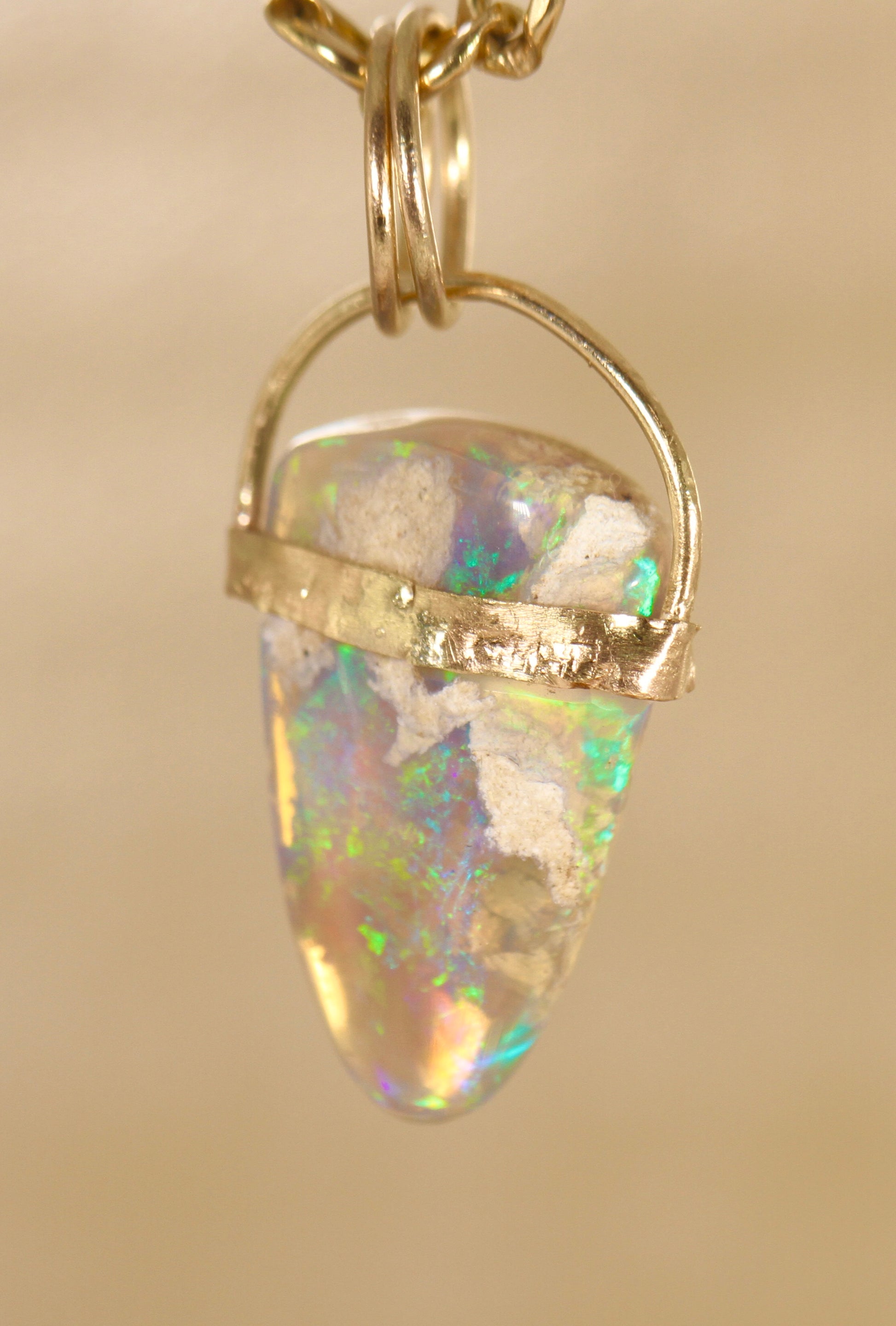 Opal pendant with gold setting on a beige background