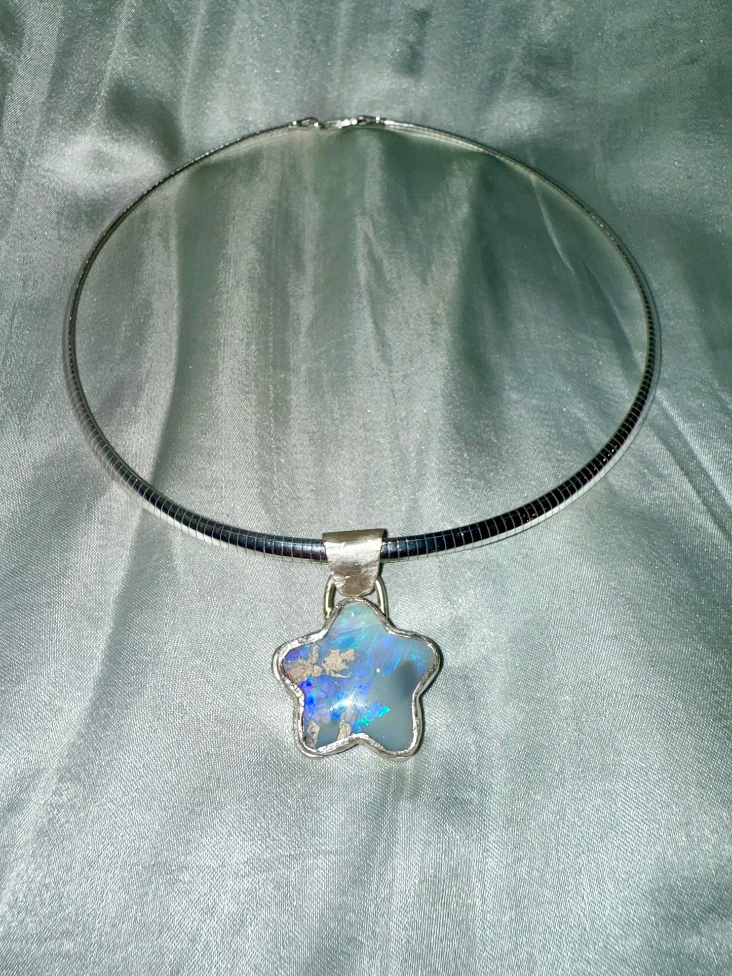 Star-shaped opal pendant on a 4mm silver omega chain against a silver satin background